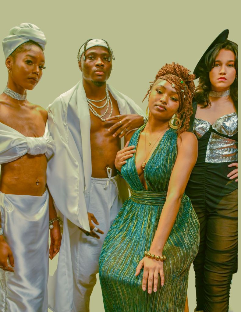 Group of four fashion models posing together, showcasing stylish outfits in front of a subtle green background.